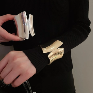 Detail of wide irregular metal bangles in polished gold and silver on black fabric