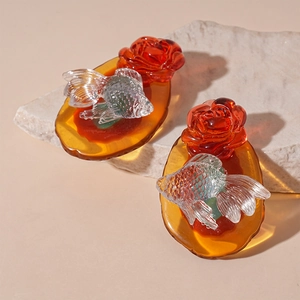 Macro shot of retro goldfish and red rose embedded in resin earrings on stone