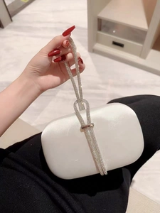 Detailed view of white satin clutch bag with elegant sparkling rhinestone knot handle