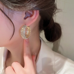 Close-up of gold C-shaped hoop earrings with sparkling pave rhinestones on a female ear