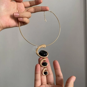 Detail showing golden choker structure with three spiral resin pendants and black stones
