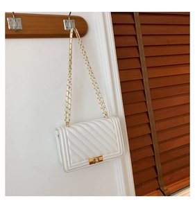 Detail of white quilted crossbody bag with gold-tone lock and chain strap on wooden hook