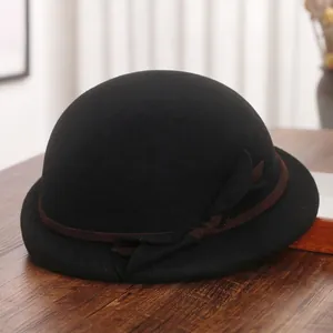 Elegant black wool felt beret with brown ribbon and bow on a rustic wooden table