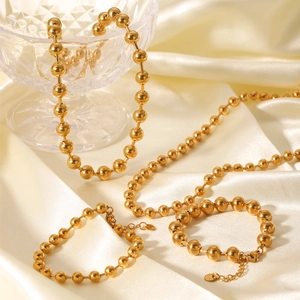 Elegantes Set aus goldener Kugelkette und Armband auf beiger Seide mit Karabinerverschluss