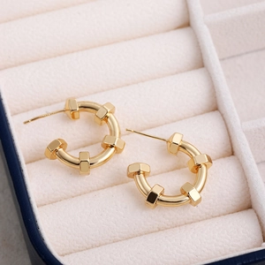 Macro shot of 18K gold plated hollow earrings with hex nut design in a beige jewelry box