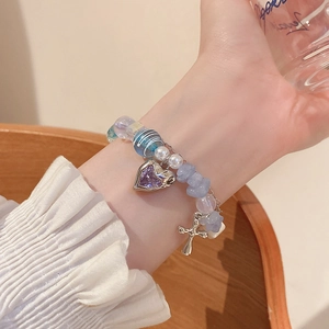 Detail of beaded bracelet with light blue stones, heart charm, and a small cross pendant