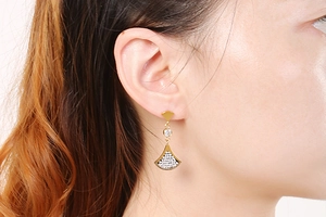 Detail of gold fan-shaped earrings with rhinestones on a model against white background