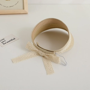 Detail of beige straw sun visor with delicate lace bow and elastic chin strap