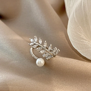 Silver open ring with zircon leaves and a white pearl on a beige silk background