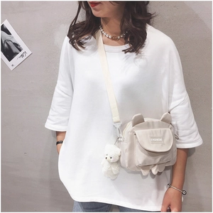 Detail view of beige canvas crossbody bag with cute bear ears and plush charm on model