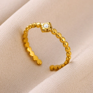 Detail of a beaded gold ring with a round clear zircon on beige velvet background