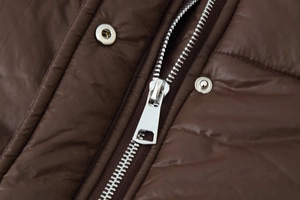 Détail d'un manteau matelassé marron café avec fermeture éclair et boutons-pression en métal