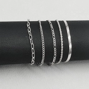 Detailed close-up of silver Figaro, paperclip, and Cuban chain bracelets on black display