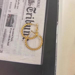 Detail of gold twisted rope hoop earrings with vintage texture on a newspaper backdrop