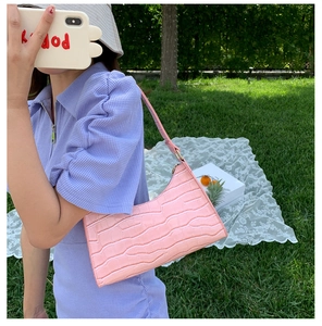 Close-up of pink faux leather baguette bag with crocodile texture and gold hardware