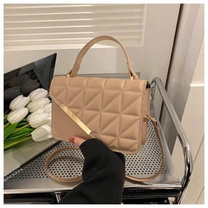 Macro detail of beige quilted handbag with gold metal bar and top handle on trolley