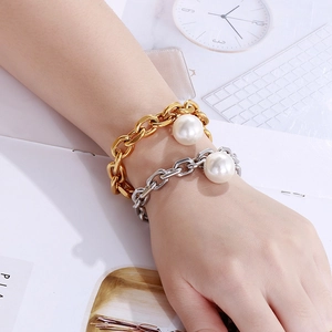 Detailed view of gold and silver thick chain bracelets with large pearl charms on wrist