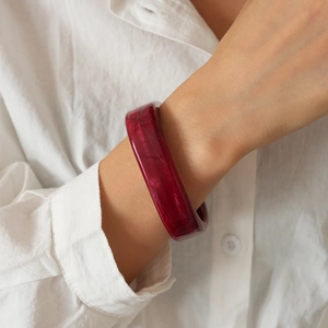 Detail view of a wide burgundy resin bangle with marble texture worn on a wrist