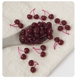 Macro view of artificial miniature cherries on a silver spoon and white textured cloth