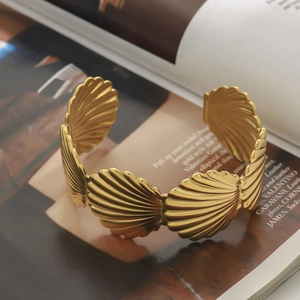 Vintage 18K gold plated stainless steel ribbed shell open bangle on a fashion magazine