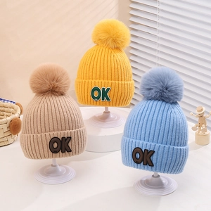Detail showing the knitted texture, fluffy pom-pom, and OK patch of these warm baby hats