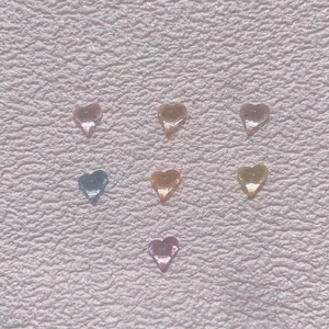 Macro shot of 7 colorful transparent heart-shaped resin nail charms on a textured pink base