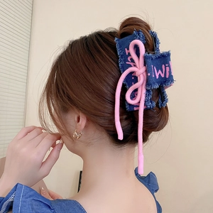 Detail of pink embroidered lettering on blue denim fabric bow hair claw clip for women