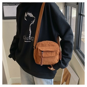 Close-up of brown corduroy crossbody bag with woven zipper pull on casual wear