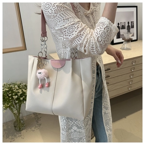 Dettaglio della borsa tote crema con tracolla in catena rosa e ciondolo a pompon soffice