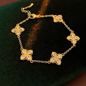 Detailed view of gold clover bracelet with five white zircon stones on green velvet backdrop