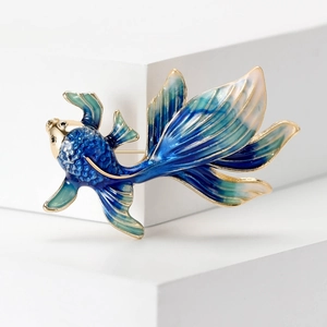 Detailed view of blue enamel goldfish brooch with golden accents on a white stand