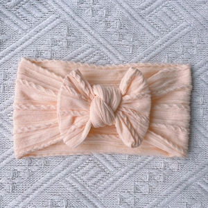 Close-up of soft cable-knit baby headband featuring a large bow in peach color
