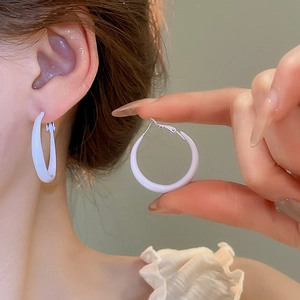 Close-up of a model wearing large white glossy hoop earrings with a minimalist finish
