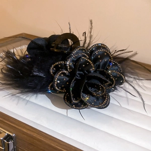 Detailed macro view of black fabric flower hair claw with feathers and rhinestones