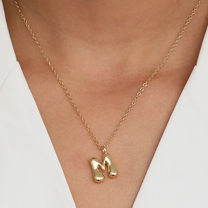 Detail showing a 3D bubble letter M pendant in shiny gold on a thin link chain necklace