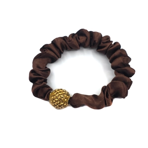 Close-up of brown satin scrunchie featuring a premium gold rhinestone-studded ball charm