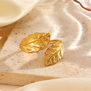 Minimalist gold leaf open ring with textured leaves on a beige travertine pedestal