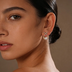 Detailed close-up of a gold cross stud earring with diamonds and a white pearl on an ear
