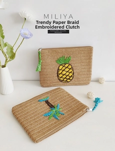 Detail of straw paper braided clutch bag featuring pineapple and palm tree embroidery
