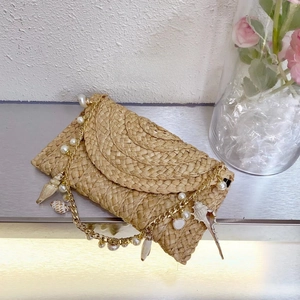 Detailed shot of handmade straw clutch bag with pearl and seashell gold chain strap