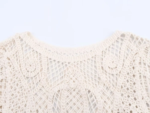 Detail of the round neckline and intricate crochet hollow-out pattern on the ivory knit top