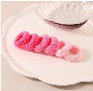 Detail of six pink braided elastic hair ties in a decorative ceramic petal tray