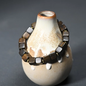 Dark brown square agarwood bracelet with gold spacers displayed on a ceramic vase