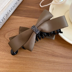 Macro detail of brown satin bow hair claw clip with grey rhinestone decoration on wood