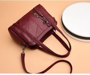 Close-up of wine red faux leather handbag with V-shaped quilting and cat pendant