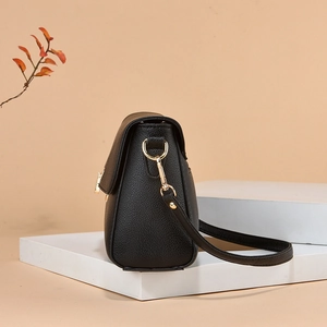 Fashionable black lychee grain leather crossbody bag with gold hardware on white stand