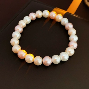 Close-up of white and pink pearls bracelet on textured dark background with warm lighting