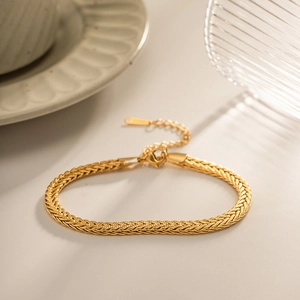 Detail of a gold braided chain bracelet with lobster clasp and extension on a beige surface