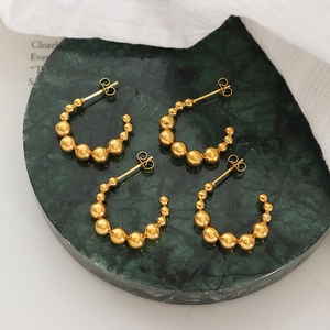 Boucles d'oreilles créoles C perlées en acier titane doré sur marbre sombre