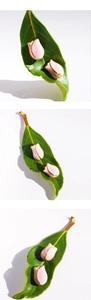 Macro detail of pink enamel tulip bud earrings with gold edges on green leaves
